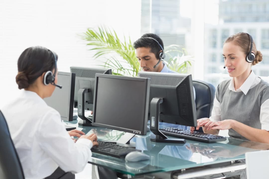 Team of customer service agents wearing headsets working at desktop computers
