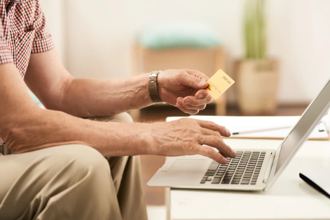 Older person using a credit card to make an online payment on laptop